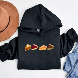 May include: Black hoodie with a graphic of four different pie slices. The slices are pumpkin, cherry, apple, and pecan.