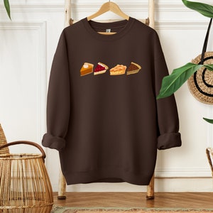 May include: A brown sweatshirt with a graphic of four different pie slices. The slices are a pumpkin pie, a cherry pie, an apple pie, and a pecan pie.
