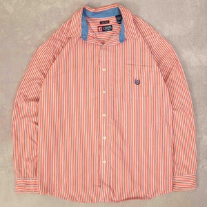 Peut inclure: Chemise à rayures verticales rouges et blanches avec un col et des poignets bleus. La chemise a une petite poche sur la poitrine gauche avec un logo. La chemise est de la marque Chaps.
