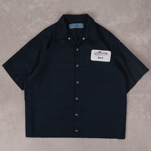 Può includere: Camicia da lavoro blu navy a maniche corte con bottoni e colletto. La camicia presenta un'etichetta bianca con il logo Hostess e il nome "Mark". La camicia è realizzata in un tessuto resistente.