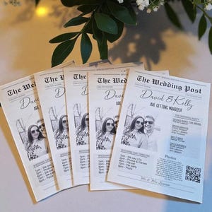 May include: A stack of wedding newspaper-style invitations. Each invitation features a photo of the couple, the text "The Wedding Post," and the names "David & Kelly." The invitations include the wedding day timeline and party details.