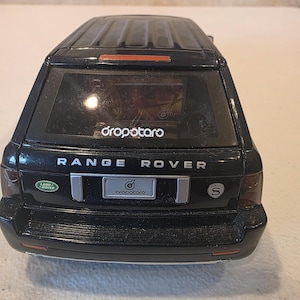 Puede incluir: Un coche de juguete Range Rover negro con el texto "Range Rover" y "dropotaro" visibles. El coche de juguete tiene un logotipo de Land Rover y el número "8" en la parte trasera.