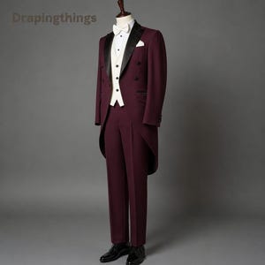 May include: A burgundy tailcoat suit featuring a white waistcoat, a white dress shirt with a white bow tie, and black dress shoes. The tailcoat has black satin lapels and a double-breasted button closure. The text Drapingthings is visible.