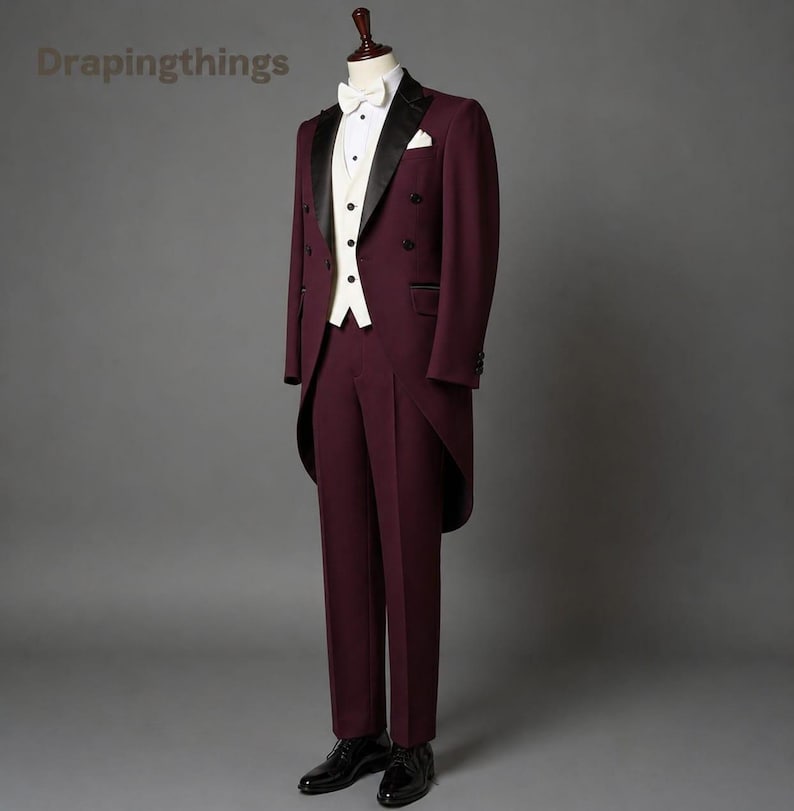 May include: A burgundy tailcoat suit featuring a white waistcoat, a white dress shirt with a white bow tie, and black dress shoes. The tailcoat has black satin lapels and a double-breasted button closure. The text Drapingthings is visible.