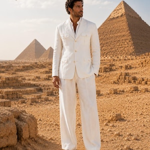 May include: A white blazer with four front pockets and matching white trousers. The blazer features a button-down front and a collared neckline. The trousers are wide-legged and full-length. The outfit is paired with a white collared shirt underneath.