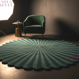 A wide shot shows a round, dark green and sage sunburst rug with a scalloped edge on the floor, accompanied by a green armchair and a studio lighting umbrella in the background.