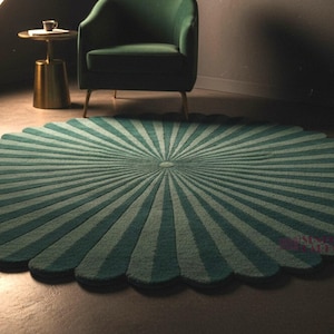 A round green rug with a scalloped edge and alternating radial sunburst stripes is laid out on a dark floor in a dimly lit room featuring a green armchair and small side table.