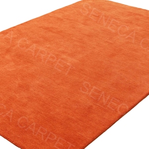 May include: A rectangular area rug in a solid, vibrant orange color with a short, dense pile texture. The surface features a repeating, semi-transparent watermark text that reads SENECA CARPET across the fabric in a diagonal orientation.