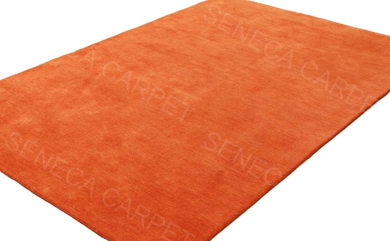 May include: A rectangular area rug in a solid, vibrant orange color with a short, dense pile texture. The surface features a repeating, semi-transparent watermark text that reads SENECA CARPET across the fabric in a diagonal orientation.