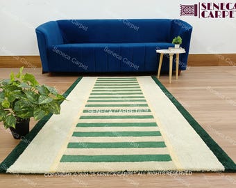 May include: A rectangular rug with a striped pattern in green and off-white. The rug has a dark green border and is placed on a wooden floor. The text "SENECA CARPET" is visible on the rug.
