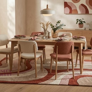 May include: A rectangular area rug featuring a wavy, abstract pattern in shades of terracotta, cream, and soft pink. The rug is placed under a light wood dining table with six chairs, alternating between cream and terracotta upholstery colors.