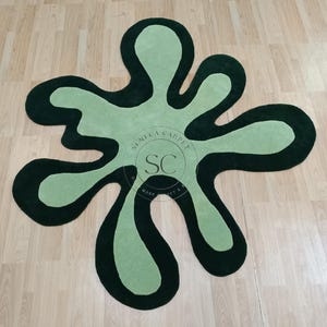 May include: A green and black abstract rug with a unique, organic shape. The rug is made of soft, plush materials and features a simple, modern design.