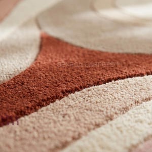 May include: A textured area rug featuring a pattern of curved, flowing lines in shades of terracotta, cream, and beige. The surface has a dense, tufted pile construction with varying heights that create a tactile, three-dimensional effect across the rug.