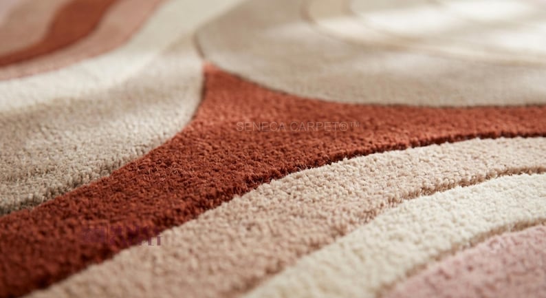 May include: A textured area rug featuring a pattern of curved, flowing lines in shades of terracotta, cream, and beige. The surface has a dense, tufted pile construction with varying heights that create a tactile, three-dimensional effect across the rug.