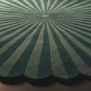 A close-up view of the textured surface of the round green rug, showing its scalloped edge and radial striped sunburst pattern meeting at a center circle.