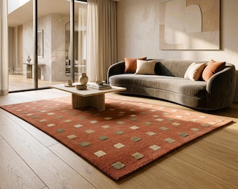 May include: A rectangular area rug featuring a deep terracotta orange base color with a repeating grid pattern of small, light beige and muted sage green squares distributed evenly across the entire surface of the floor covering.