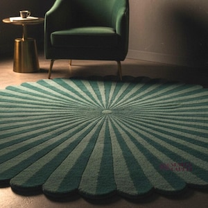A vertical-oriented photo of the round scalloped rug with dark green and lighter green radial stripes, positioned in front of a green armchair on a dark floor.