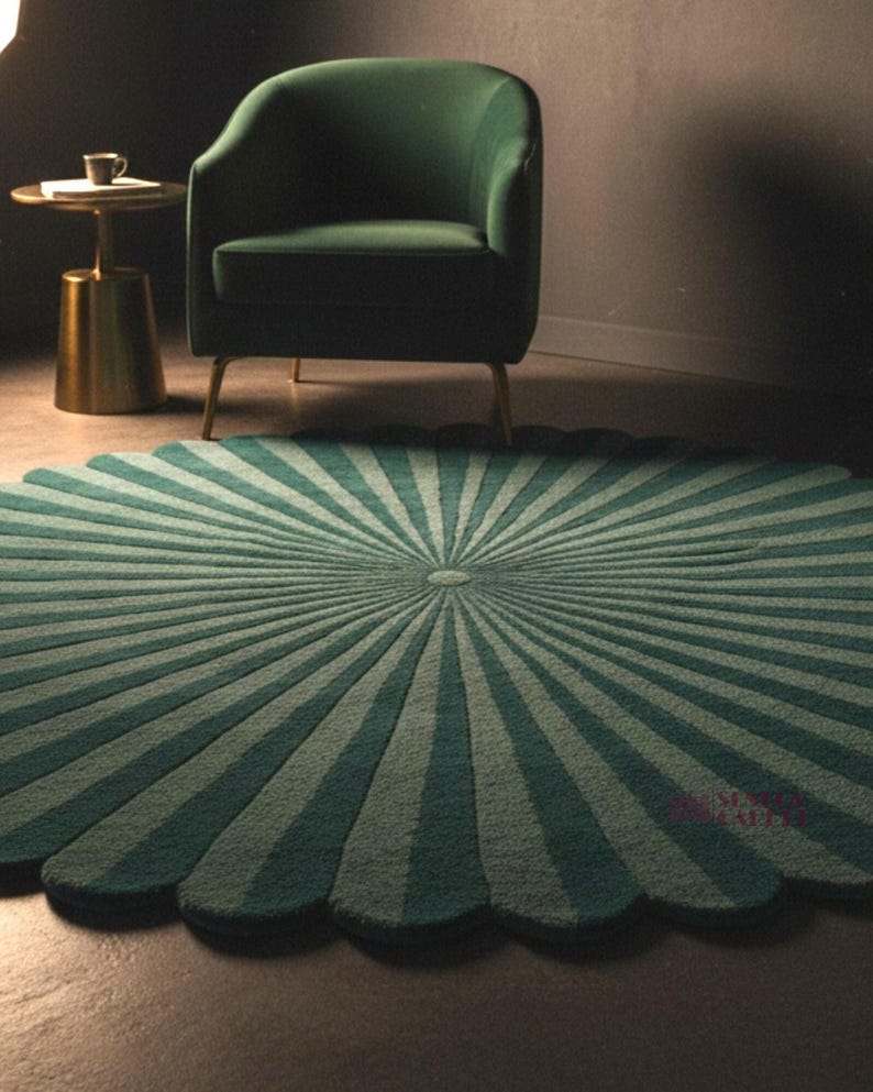 A vertical-oriented photo of the round scalloped rug with dark green and lighter green radial stripes, positioned in front of a green armchair on a dark floor.