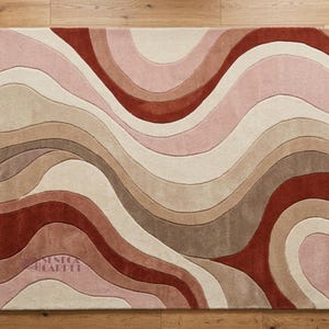 A top-down view of a rectangular rug with wavy abstract patterns in shades of pink, terracotta, and beige.