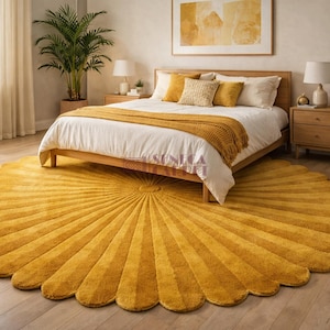 A mustard yellow scalloped round rug with a sunburst pattern lies on a light wood floor in a bedroom with a bed and nightstands.