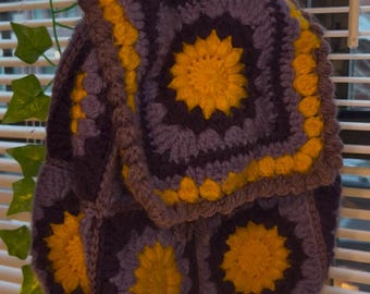 May include: A purple and yellow crocheted backpack with a floral design. The backpack is made of yarn and has a square shape.