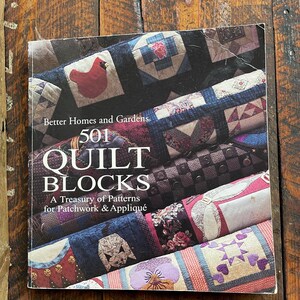 May include: A book titled "501 Quilt Blocks" by Better Homes and Gardens. The cover displays a colourful patchwork quilt design with various patterns and colours. The book is for patchwork and appliqué.