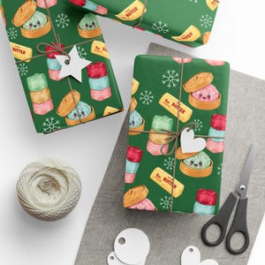 Könnte beinhalten: Dunkelgrünes Geschenkpapier mit einem wiederkehrenden Muster aus niedlichen Cartoon-Teigtaschen in Bambusdämpfern, Stapeln bunter Marshmallows und gelben Butterstücken mit der Aufschrift 4oz. BUTTER, verziert mit weißen Schneeflocken.