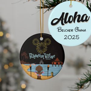 May include: Two round Christmas ornaments hanging from gold strings. One is light blue with the word "Aloha", the name "Belcher Ohana", and the year "2025". The other is black with a Polynesian Village Resort scene, fireworks, and text.