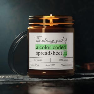 Könnte beinhalten: Ein braunes Glasgefäß mit einer Kerze und einem weißen Etikett mit der Aufschrift "The calming scent of a color coded spreadsheet". Das Etikett enthält auch die Texte "Soy Candle", "Cotton Wick", "since 2025", "100% natural" und "Vegan non toxic".