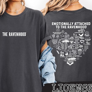 Peut inclure: T-shirt gris foncé avec le texte "THE RAVENHOOD" sur le devant. Le dos du t-shirt présente le texte "EMOTIONALLY ATTACHED TO THE RAVENHOOD" au-dessus d'un graphique en forme de cœur avec des illustrations et du texte. Le mot "LICENSED" est en bas.