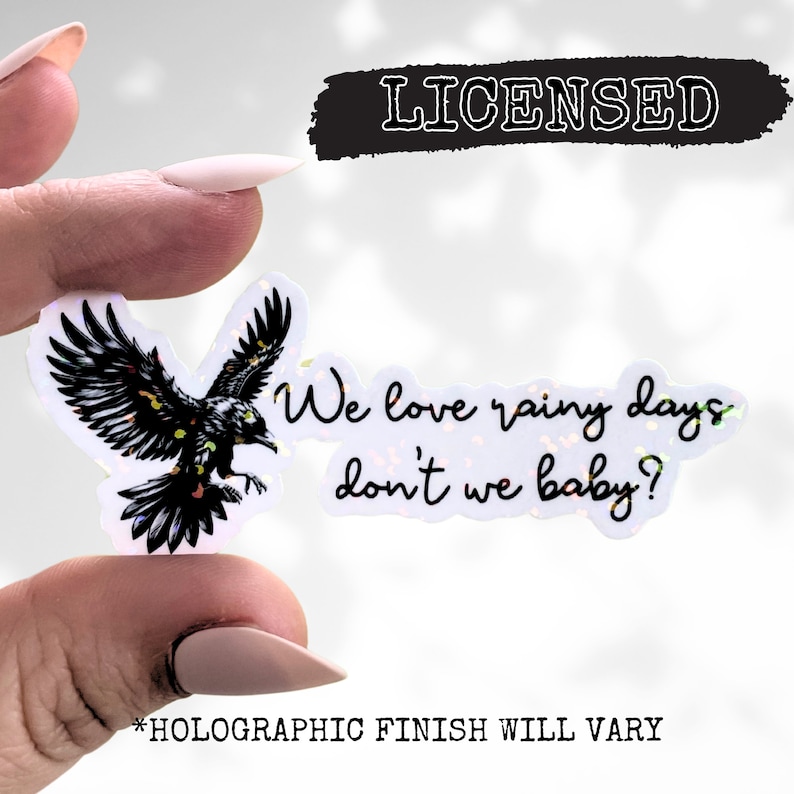 May include: A holographic sticker with a black raven flying and the text "We love rainy days don't we baby?"