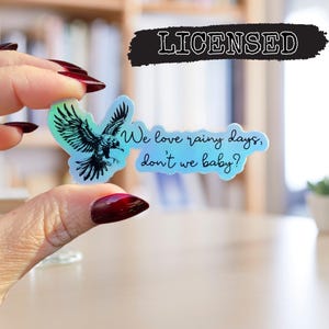 May include: A holographic sticker with a black silhouette of a bird and the text "We love rainy days, don't we baby?"