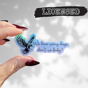 May include: A holographic sticker with a black and white illustration of a bird flying with the text "We love rainy days, don't we baby?"