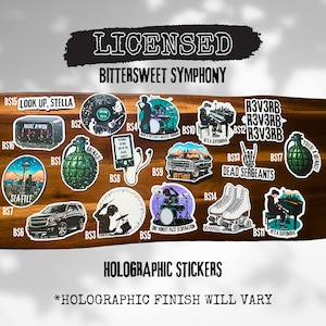 Peut inclure: Un ensemble de 17 autocollants holographiques présentant divers motifs, dont une grenade, une batterie, un crâne et un paysage urbain. Les autocollants sont tous sur un fond en bois et ont une finition holographique. Le texte "Licensed Bittersweet Symphony" est en haut de l'image. Le texte "Holographic Stickers" est au milieu de l'image. Le texte "*Holographic Finish Will Vary" est en bas de l'image.