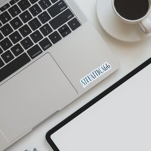 May include: A silver laptop computer with a black keyboard and a white sticker on the trackpad that says "STFUATTDLAGG".
