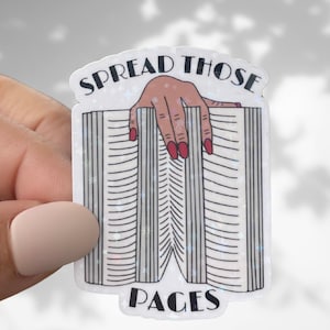 May include: A white sticker with a hand holding open a book. The sticker says "Spread Those Pages" in black text.