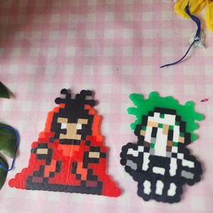 May include: Two pixel art figures. One is a red and black figure with a tan face. The other is a black and white figure with green hair. Both figures are made of small, colorful beads.