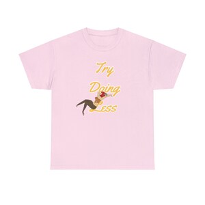 Könnte beinhalten: Pinkes T-Shirt mit einer gelben Grafik, auf der "Try Doing Less" steht, und einem Cartoon-Bild einer Frau.