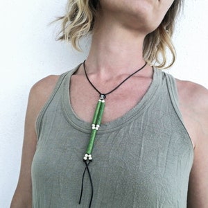 May include: A green and white beaded necklace with a leather cord. The necklace has a silver clasp and hangs down the front of the wearer's chest.