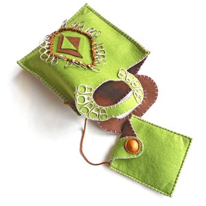 May include: A green felt bag with a brown felt flap and a decorative design of silver metal rings and brown felt shapes. The bag has a white stitch detail and a small matching green felt pouch with a brown button.