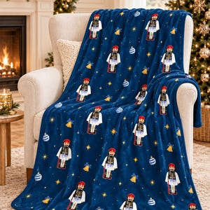 May include: A deep blue plush throw blanket featuring a repeating pattern of nutcracker figures wearing red hats and white uniforms, interspersed with gold bells, blue and white striped ornaments, and small yellow stars across the fabric.