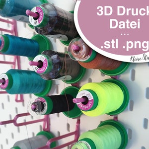 May include: A white pegboard with a pink metal rack holding spools of thread in various colours, including teal, green, yellow, brown, and grey. The text "3D Druck Datei .stl .png" is on a pink circle in the top right corner of the image.