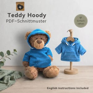 Könnte beinhalten: Ein brauner Plüsch-Teddybär in einem blauen Kapuzenpullover mit Fronttasche, daneben ein passender blauer Kapuzenpullover auf einem Holzkleiderbügel. Der Text lautet Teddy Hoody PDF-Schnittmuster, Einfach nähen und English instructions included.