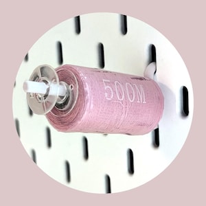 May include: A pink spool of thread with a white plastic bobbin and a white hook. The spool is labeled "500M".