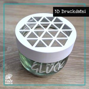 Puede incluir: Un tarro de cristal transparente con una tapa geométrica blanca. El tarro contiene un líquido verde y tiene la palabra "GLÜCK" impresa. El texto "3D Druckdatei" está en un rectángulo negro en el fondo.