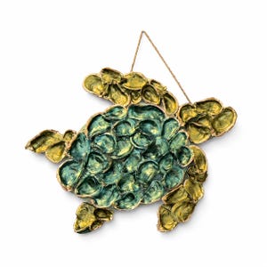 May include: A wall hanging shaped like a sea turtle, constructed from numerous individual oyster shells. The central shell area is painted in shades of teal and blue, while the flippers and head are finished in a metallic gold tone.