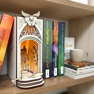 Könnte beinhalten: Ein hölzerner Buch-Nook mit einer beleuchteten Szene zum Thema Quidditch. Das Design umfasst einen goldenen Schnatz und einen Besen, mit den Worten "Harry Potter" auf den Buchrücken. Der Nook steht auf einem Holzregal mit anderen Büchern.