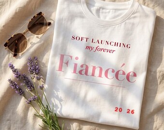 Camiseta de lanzamiento suave de Prometida 2026, estética cinematográfica moderna, con degradado rosa granulado