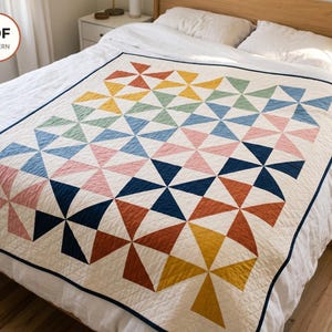 Puede incluir: Una colcha con un patrón repetitivo de molinillos en tonos amarillo mostaza, verde salvia, azul claro, rosa empolvado, azul marino y naranja terracota sobre un fondo crema con un borde azul marino y acolchado de diamantes.