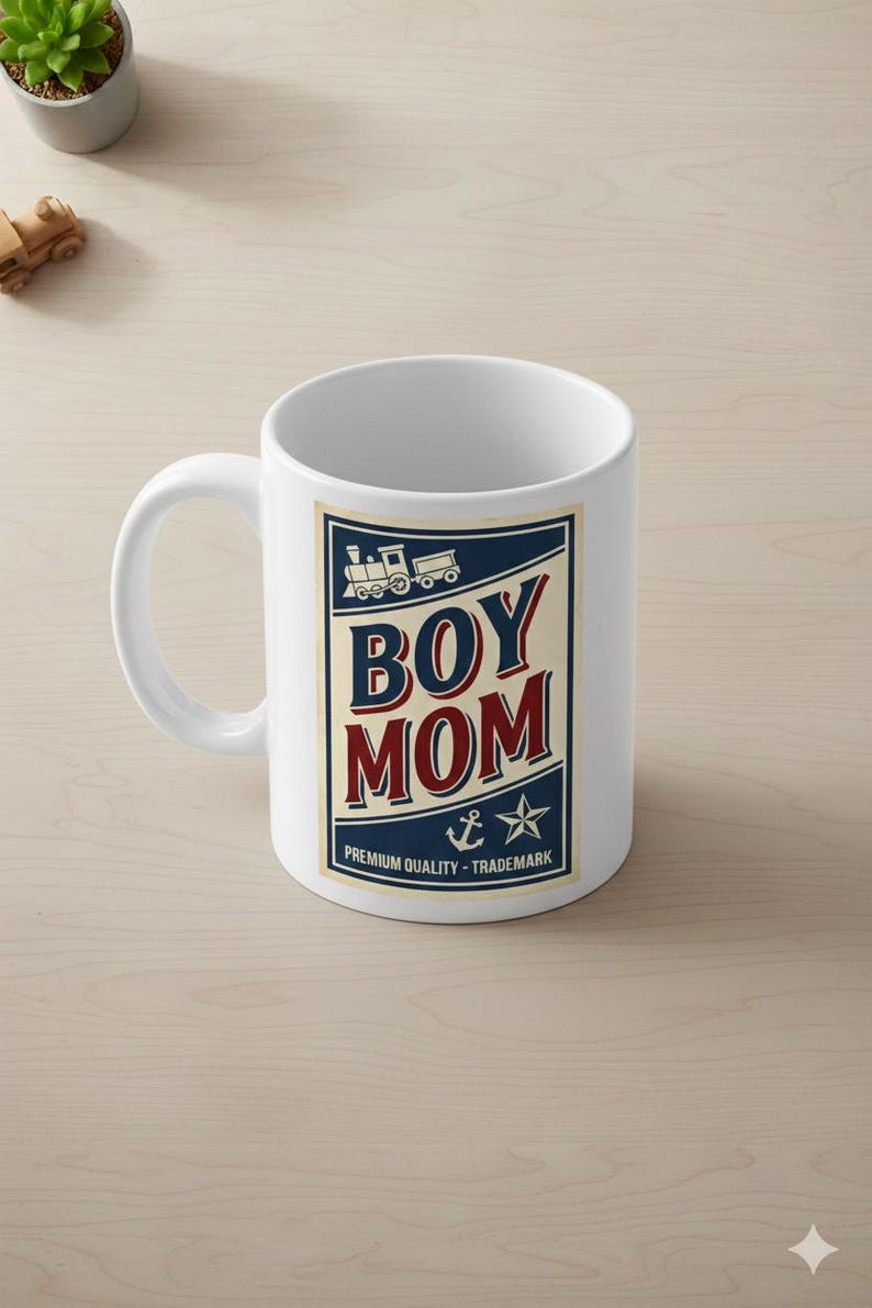 Puede incluir: Taza de cer&aacute;mica blanca con un gr&aacute;fico azul, rojo y crema que dice "BOY MOM". El dise&ntilde;o incluye un tren, un ancla y una estrella. Tambi&eacute;n se incluye el texto "PREMIUM QUALITY - TRADEMARK".
